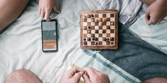 spelers rond bordspel met schaakbord en smartphone op deken