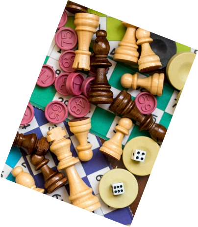 Verspreide schaakstukken, bingokaarten, roze speelchips en dobbelstenen zorgen voor een speelse mix van strategie en toeval, kleurrijk en levendig.